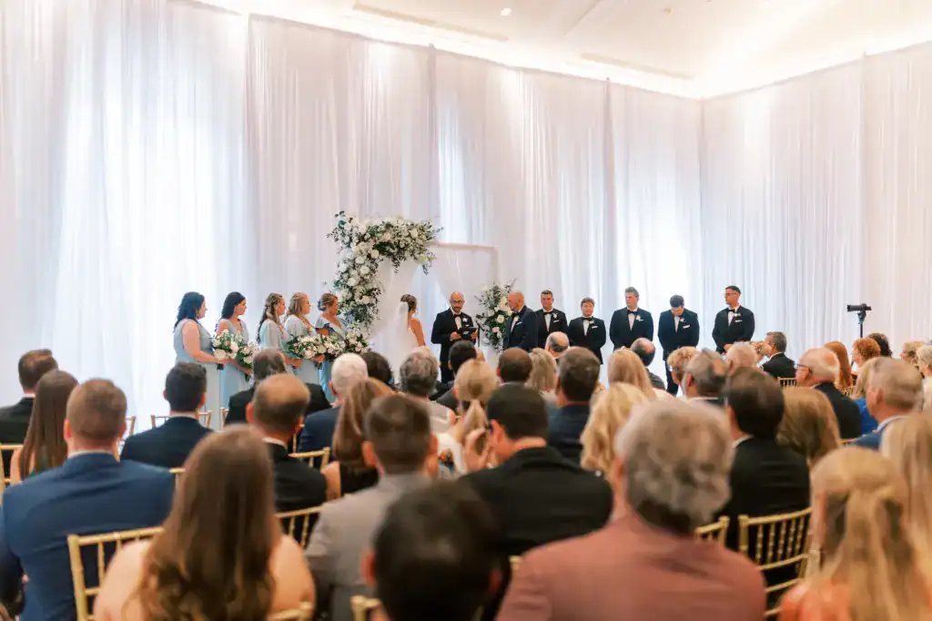 Ceremony at The Vinoy with a full-height ivory drape wall behind the altar and rows of gold Chiavari chairs