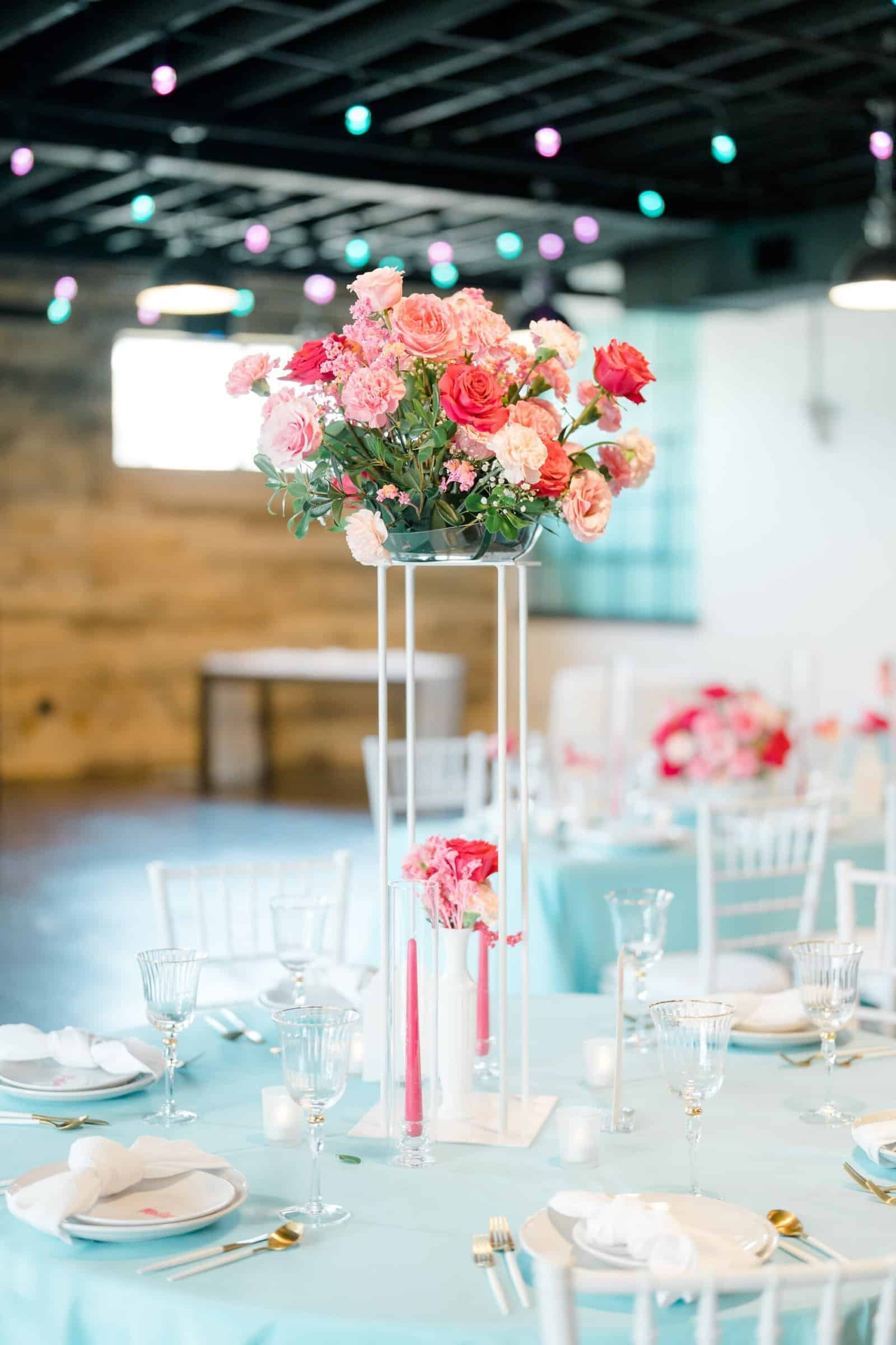Elegant table setting featuring white plates, gold-rimmed glassware, and vibrant pink floral centerpieces.