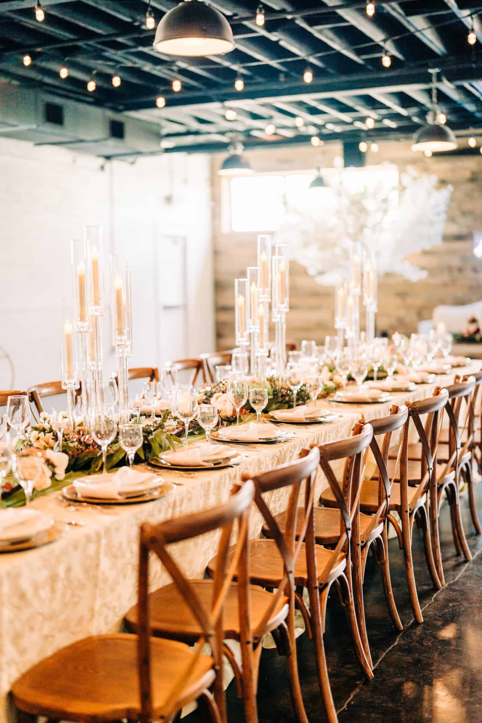 Long banquet table under ivory crushed velvet linen with glass candelabra in the industrial room at The West Events