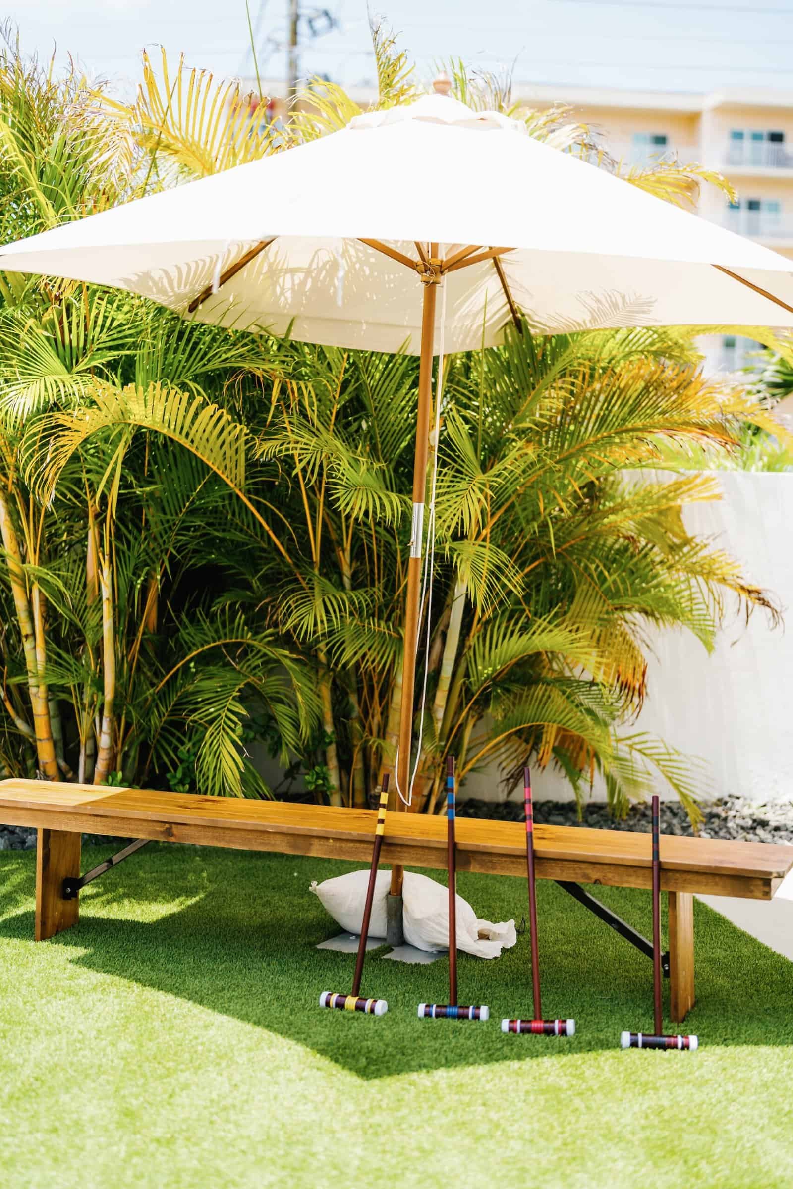 Cream market umbrella and wooden bench on the lawn with a croquet set at The West Events