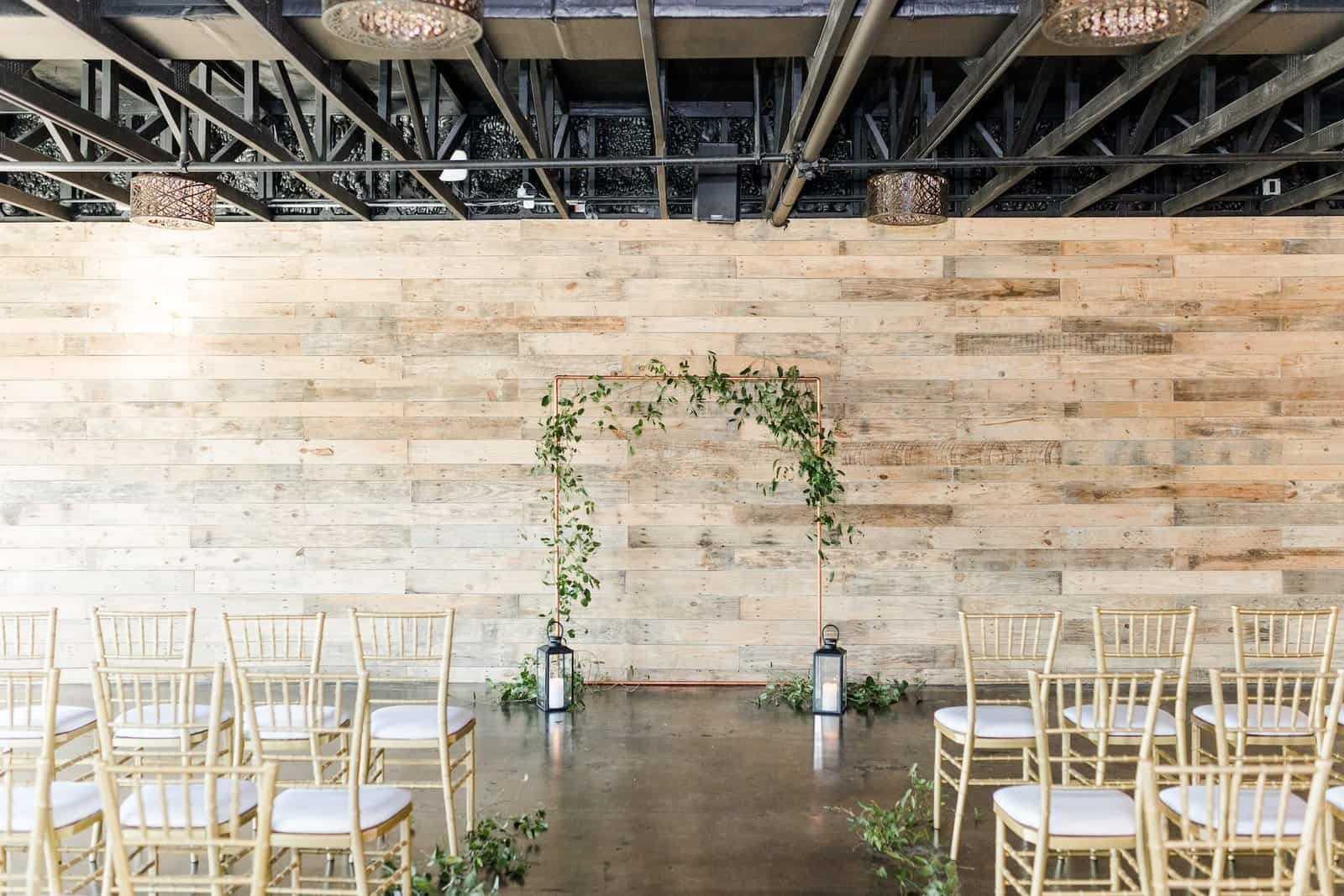 Rows of gold Chiavari chairs facing a copper arch in the industrial room at The West Events Space