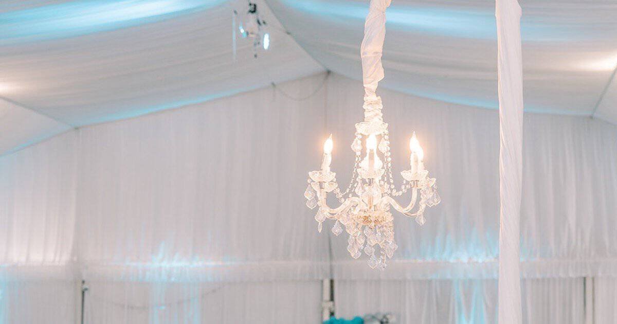Crystal chandelier with candle-style lights hanging from a white draped ceiling washed in soft blue uplighting