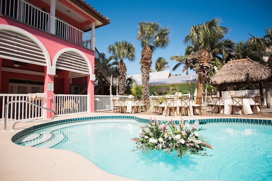 Poolside Wedding Reception Setting with Wood Chairs and Tropical Foliage Centerpieces