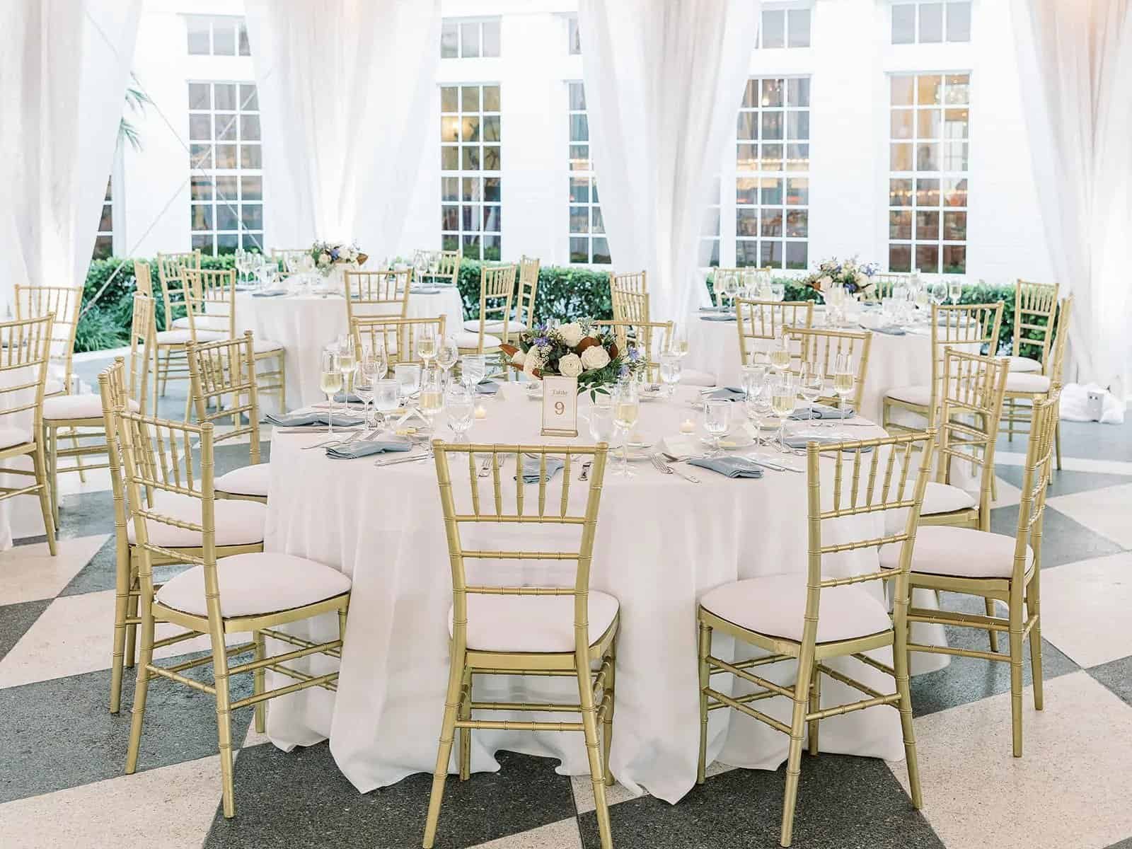 Round reception table with gold chiavari chairs, blush linen and blue embroidered napkins