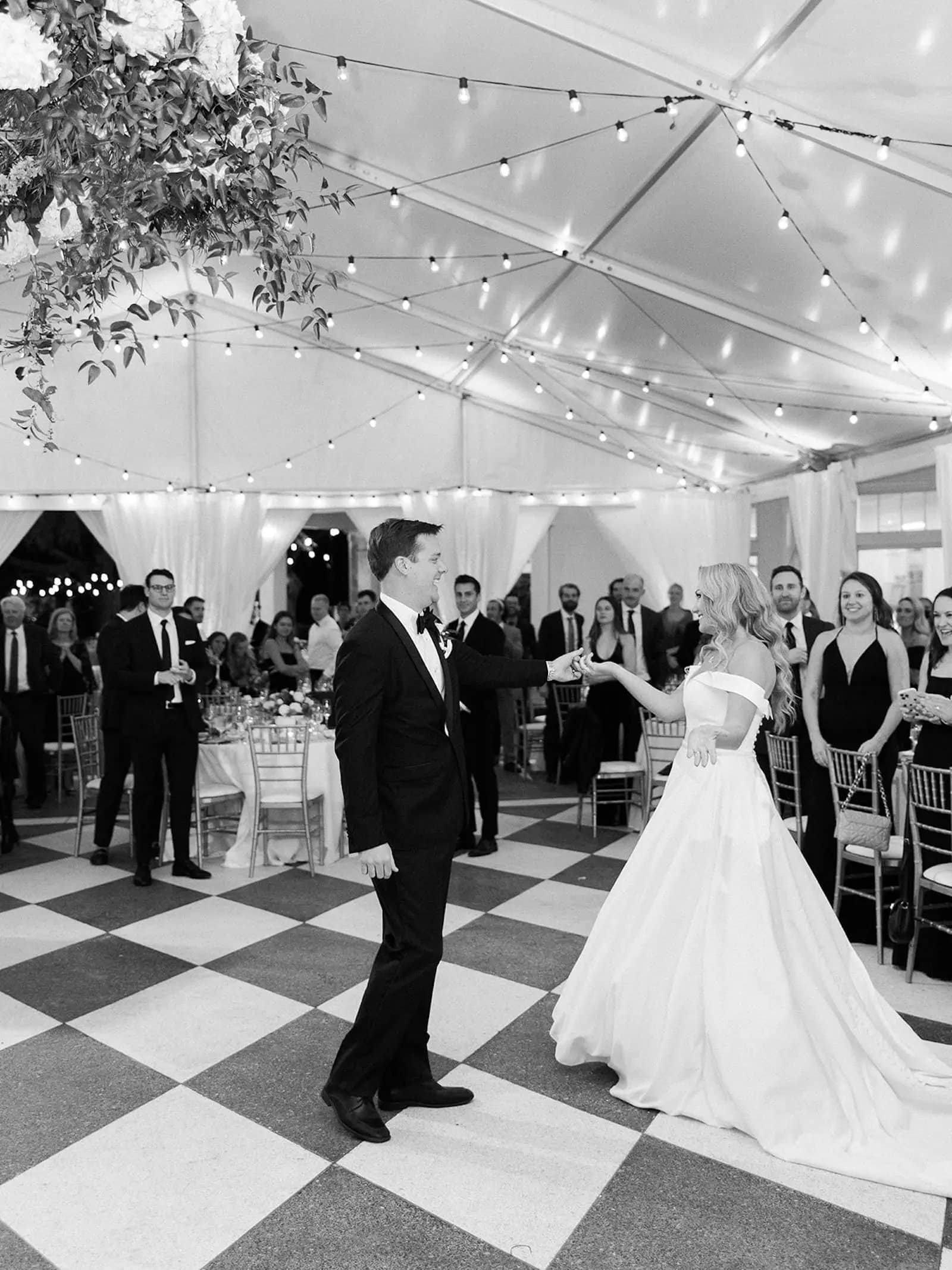 Bride and groom dancing beneath string lights at their tented waterfront reception