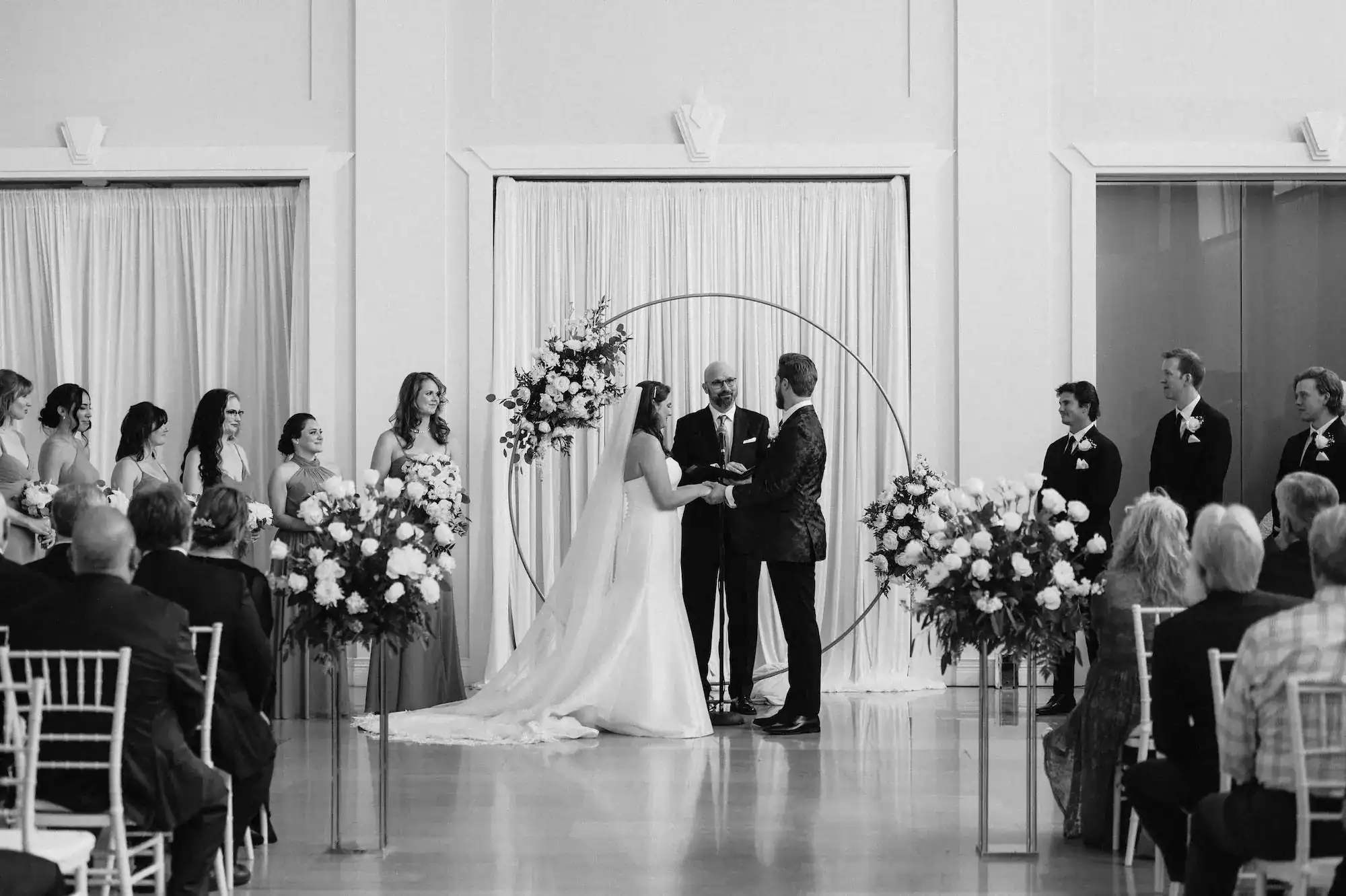 Bride and Groom Exchanging Vows in front of Circular Gold Floral Arch and Draping at The Vault