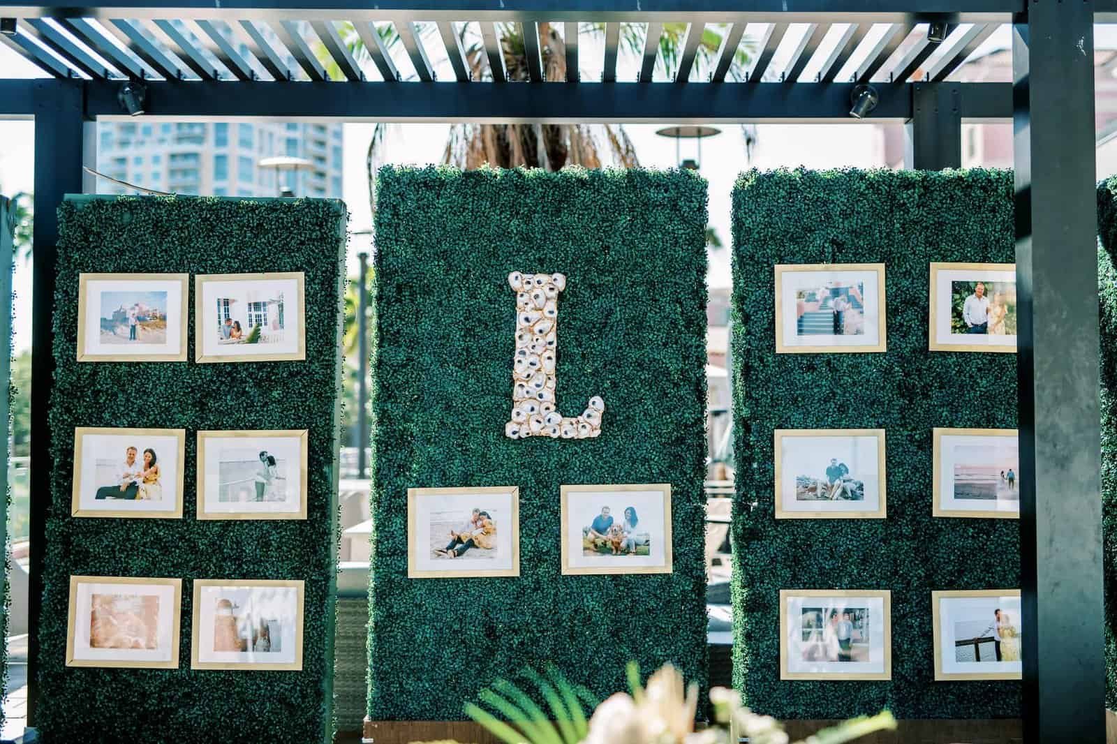 Green boxwood hedge walls displaying framed photographs and a monogram initial under a pergola